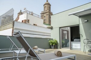 Una terraza en la azotea con sillones de descanso, una planta en maceta y vistas a una torre histórica.
