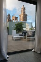 Un balcon offrant une vue sur un bâtiment historique doté de deux tours avec clochers, un espace extérieur avec des sièges blancs et un pot de fleurs.