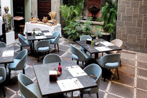 Un restaurant doté de nombreuses tables et chaises, d’une fontaine et de plantes en pot.