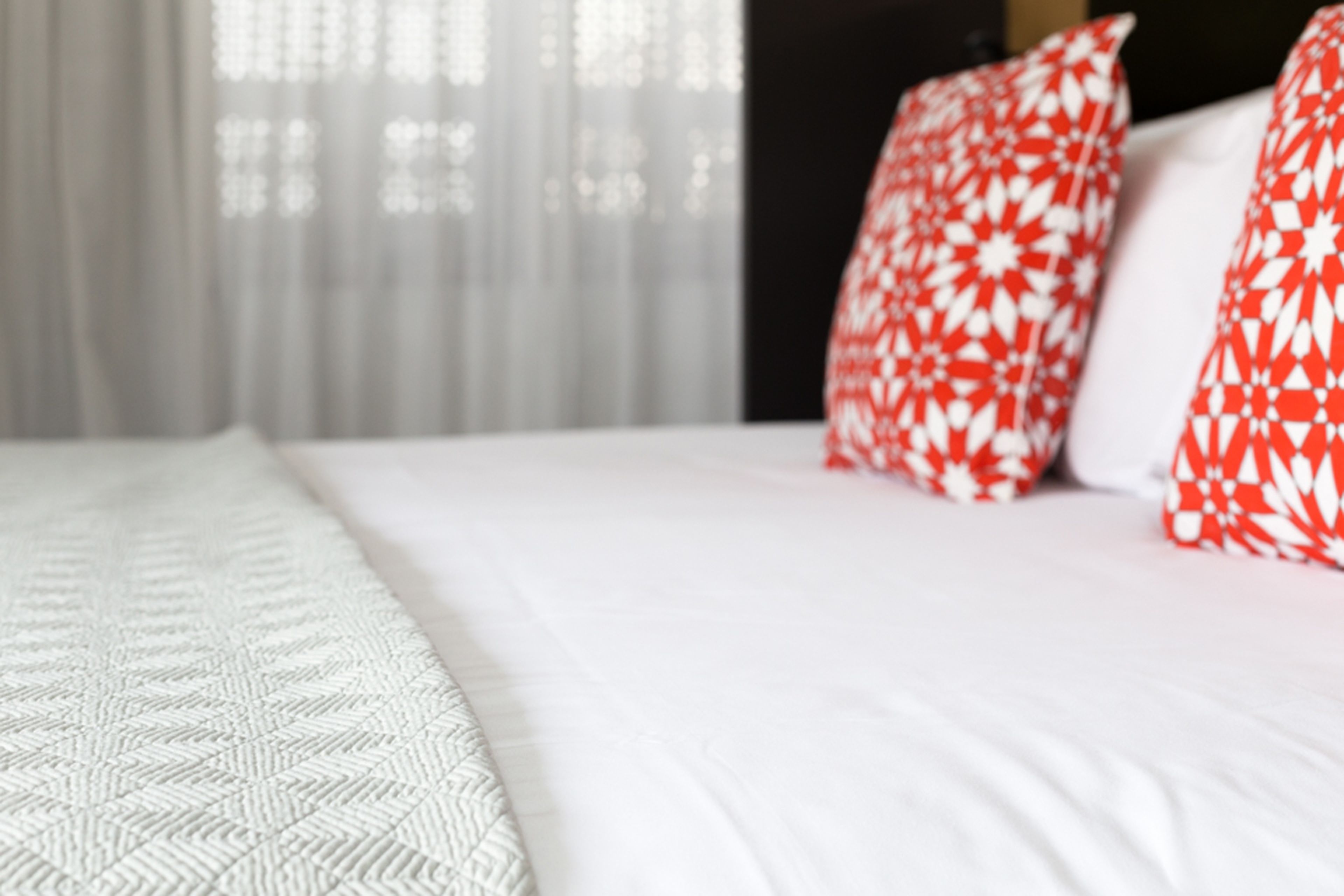 A bed with white bedding and red and white patterned pillows.