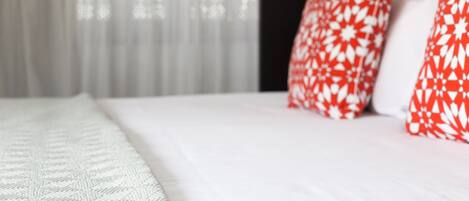 A bed with white bedding and red and white patterned pillows.