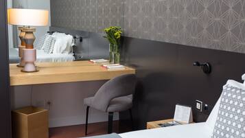 A hotel room with a bed, a desk with a lamp, a chair, a vase with flowers, and a bedside table with a menu.