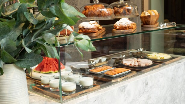Mostrador de una pastelería con pasteles y postres, una vitrina de cristal y una planta en maceta.