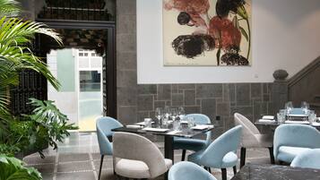 A dining area with tables set for two, chairs, and a large abstract painting on the wall.