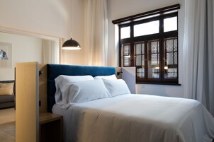 Un dormitorio con cama, mesita de noche, lámpara, ventana con persianas y puerta.