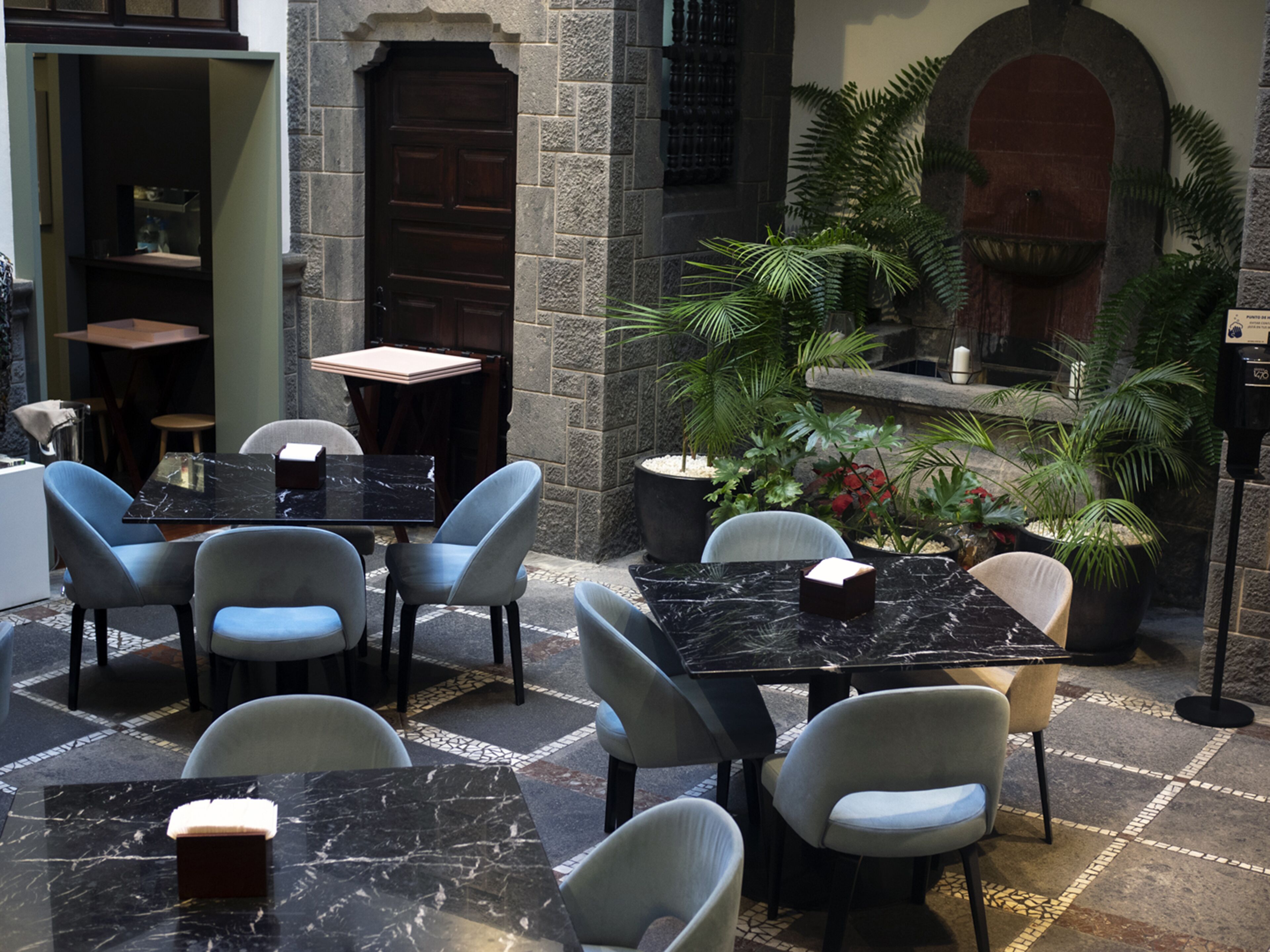 An outdoor patio area with marble-topped tables and chairs, surrounded by stone walls and potted plants.