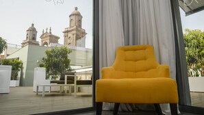 Un sillón amarillo en una habitación moderna con un ventanal que da a un edificio histórico con cúpulas.