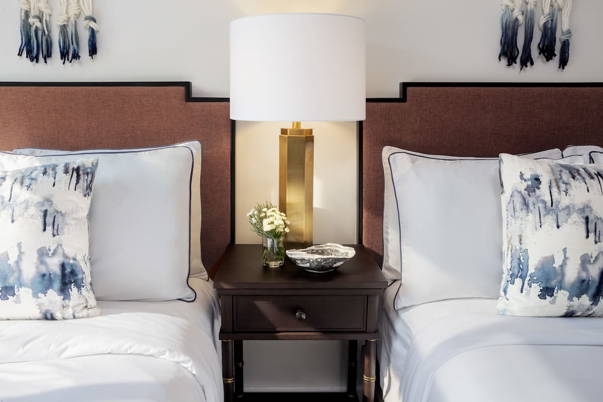 A hotel room with two beds, a nightstand with a lamp, and a vase with flowers.