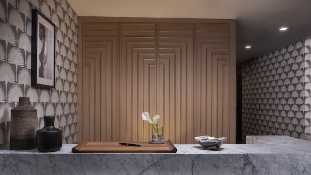 A reception desk with a wooden panel backdrop, a framed photo, and a vase with flowers. - Redford Hotel (New York)