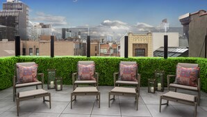 A rooftop terrace with four wicker chairs and a bench, a green hedge, and a cityscape view. - Redford Hotel (New York)