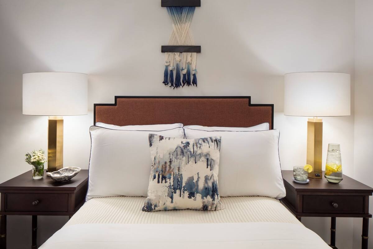 A hotel room with a bed, two bedside tables, a wall-mounted macrame piece, and two lamps.