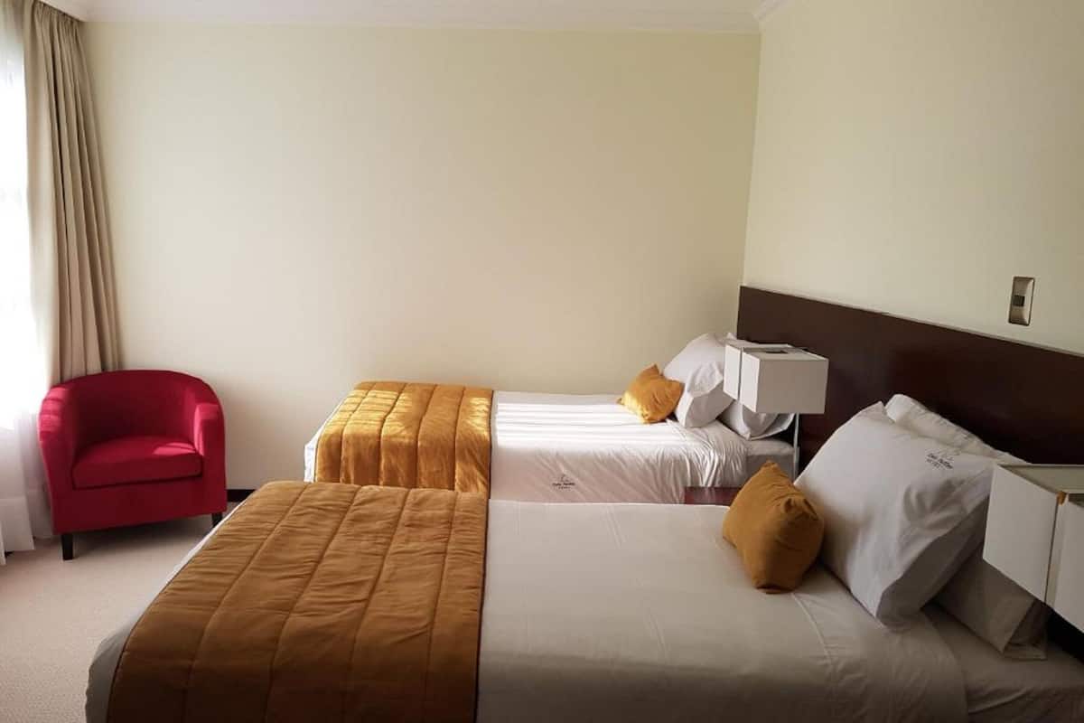 Une chambre d’hôtel avec deux lits, une chaise rouge et une table de chevet avec une lampe.