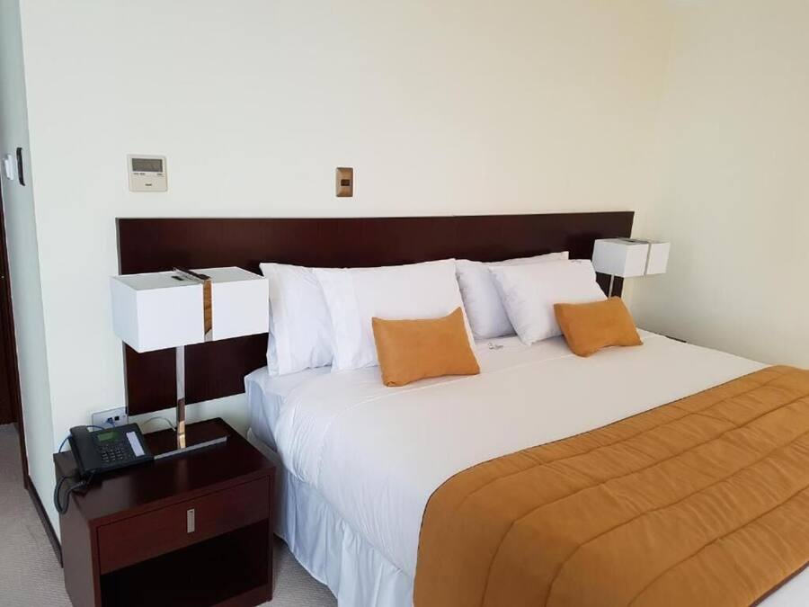 A hotel room with a large bed, two bedside tables, a nightstand, a wall-mounted thermostat, and a telephone.