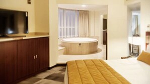 A hotel room with a bed, a TV, a wooden cabinet, and a bathtub.