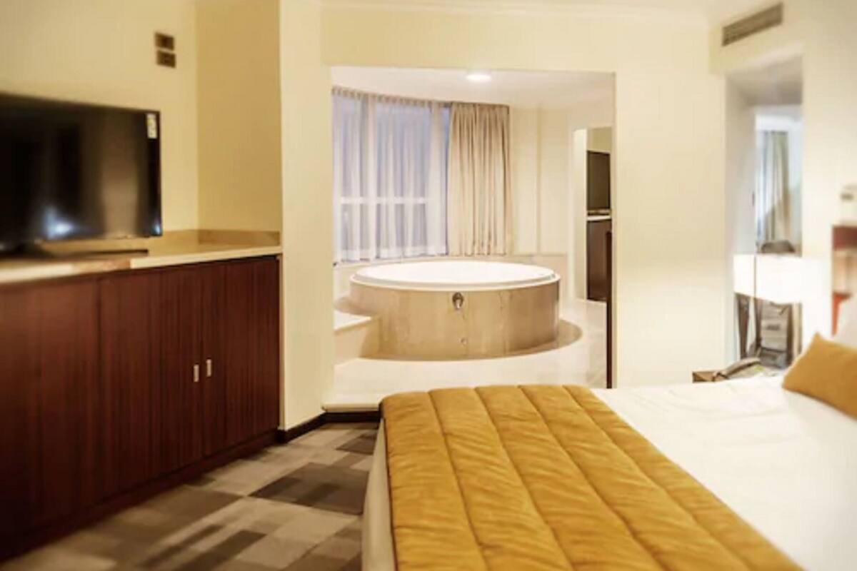 Une chambre d’hôtel avec un lit, une télévision, une armoire en bois et une baignoire.