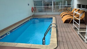 A pool area with a clear blue pool, wooden deck, and yellow lounge chairs.