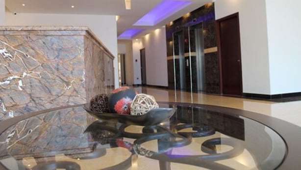A modern lobby with a marble reception desk, a glass coffee table with decorative items, and a glass elevator.