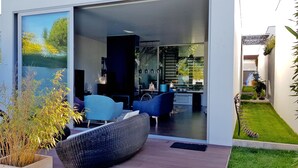A modern house with a glass door leading to a living area with blue chairs and a dining area. - Father's House Beach House (Sesimbra)