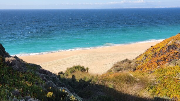 A coastal landscape with a sandy beach, clear blue sea, and rocky cliffs. - Father's House Beach House (Sesimbra)