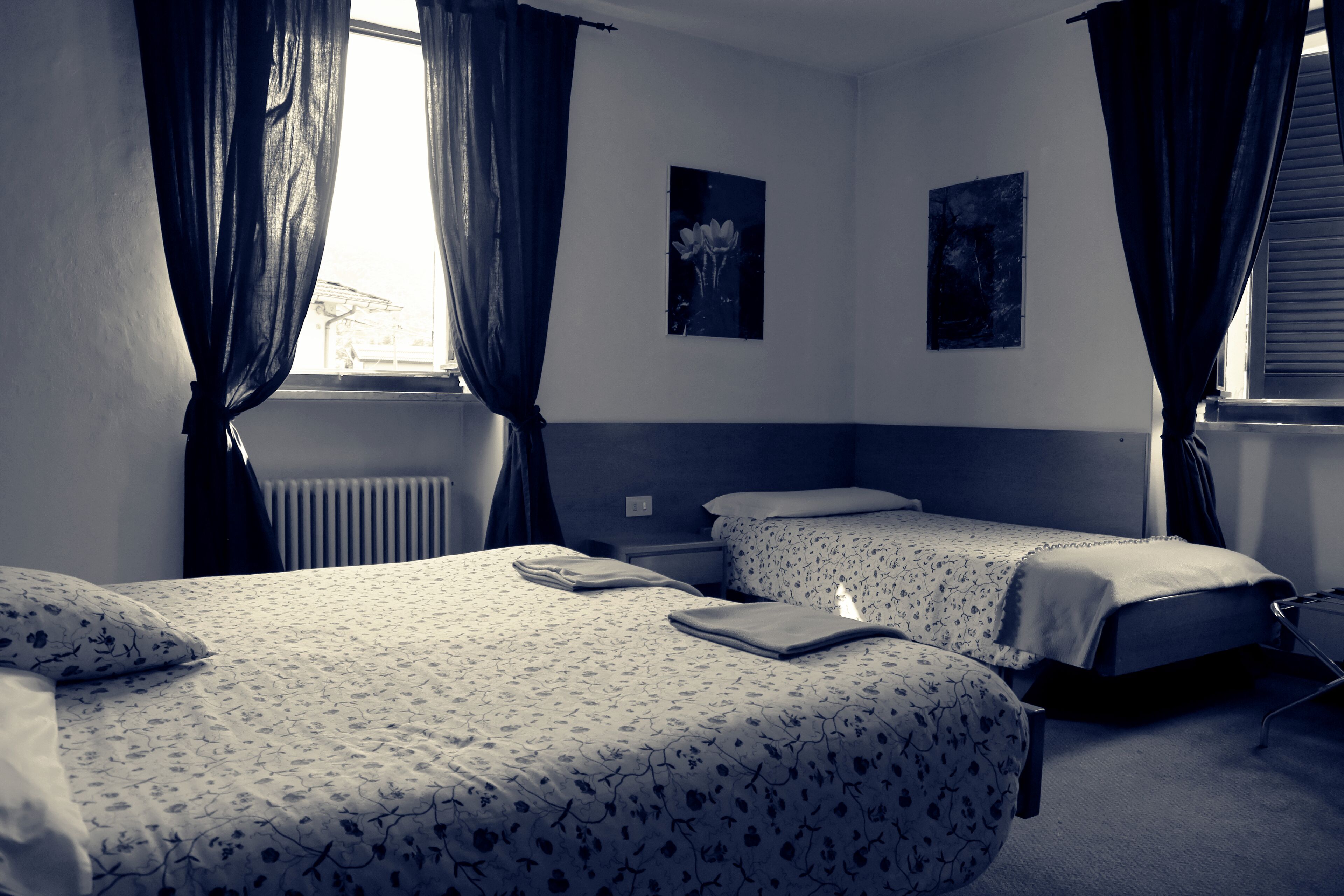 A hotel room with two beds, a radiator, and two framed pictures on the wall.