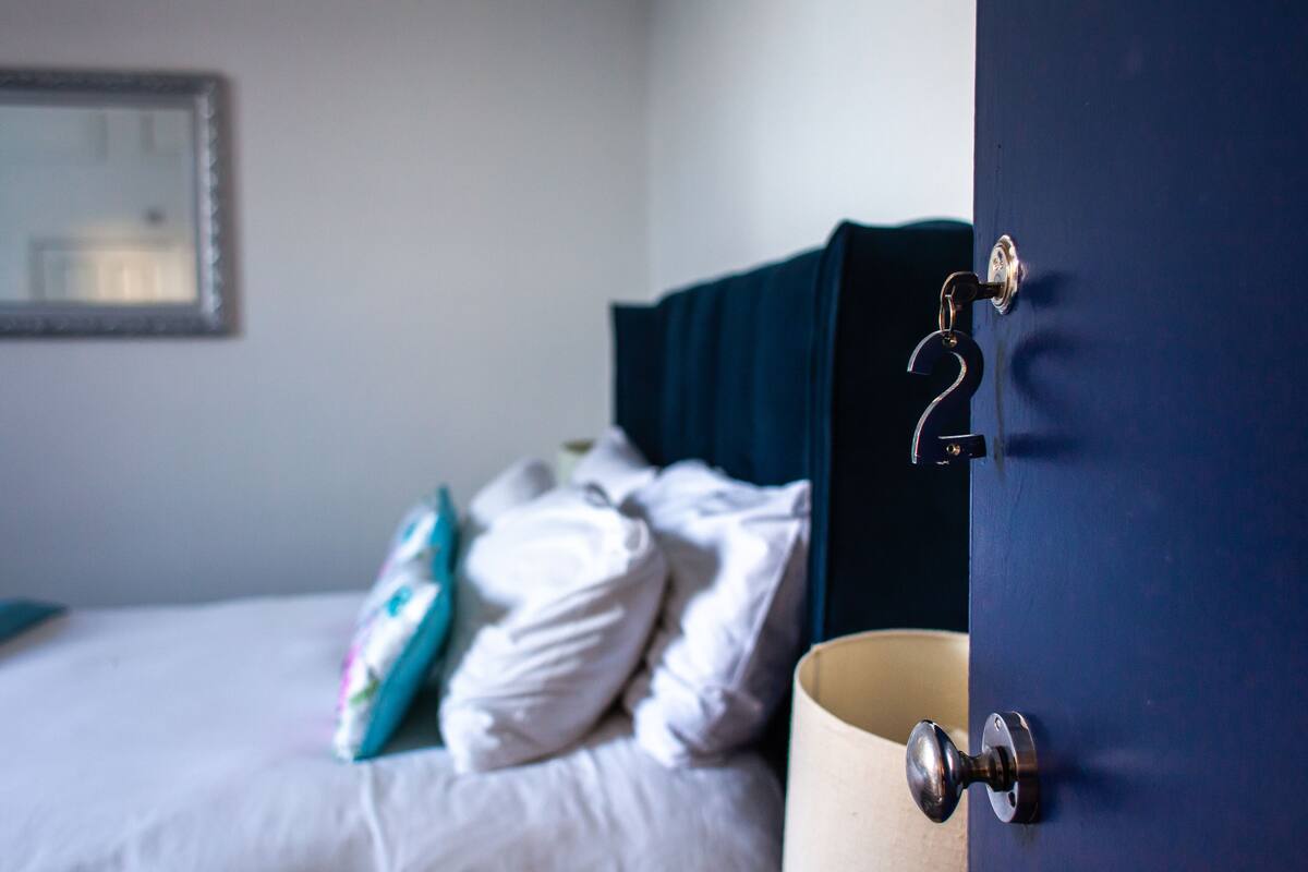 A hotel room with a bed, a dark-colored door, and a visible number '2' on the door handle.