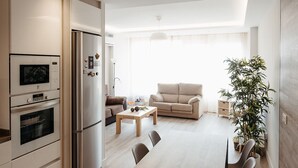 A modern kitchen with built-in appliances, a dining area with a table and chairs, a sofa, and a large window providing natural light. - DUPLEX IN GRAN VIA, GARAGE AND WIFI (Logroño)