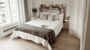 A modern bedroom with a large bed, a bedside table with a lamp, and a view of the city through the window. - DUPLEX IN GRAN VIA, GARAGE AND WIFI (Logroño)