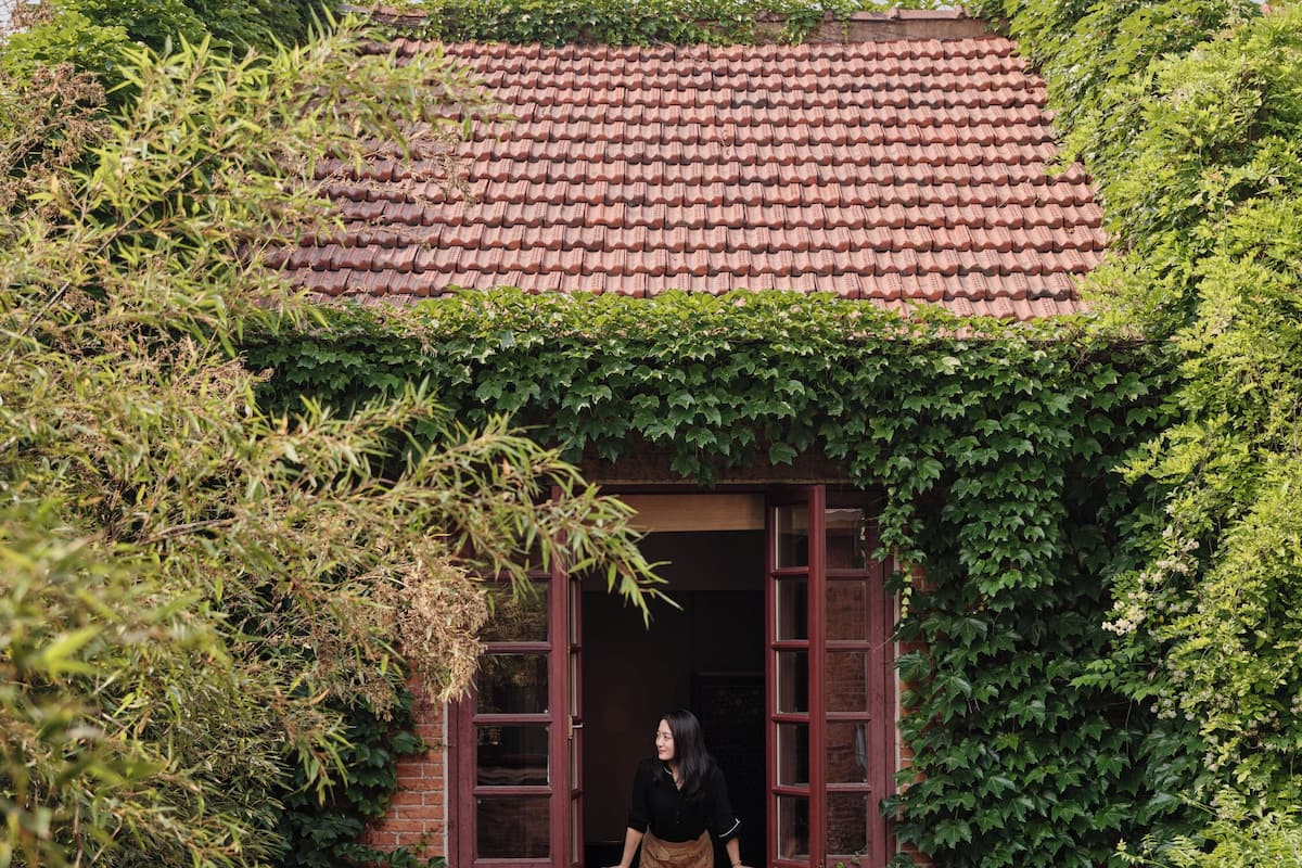A house with a red-tiled roof, partially covered in green ivy, and a window with a person standing inside.