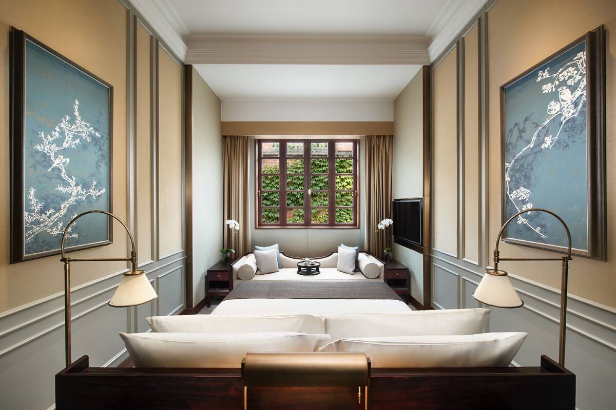 A spacious bedroom with a large bed, two bedside tables, a TV, and a window with curtains.