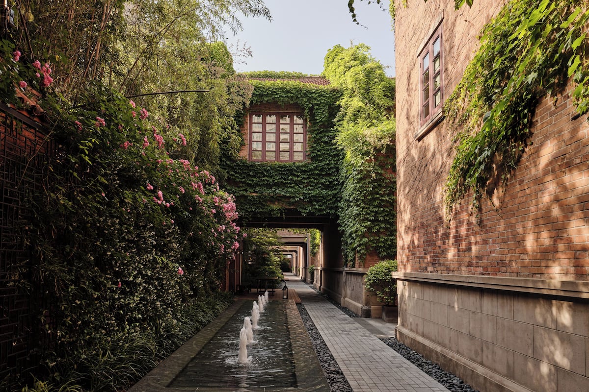 A narrow alley with a water feature, brick walls, and greenery.