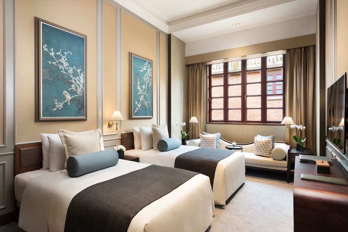 A hotel room with two beds, a sofa, a TV, and artwork on the walls.