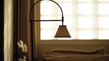 Una cama con cubre blanco, una mesita de noche con lámpara y una ventana con persianas.