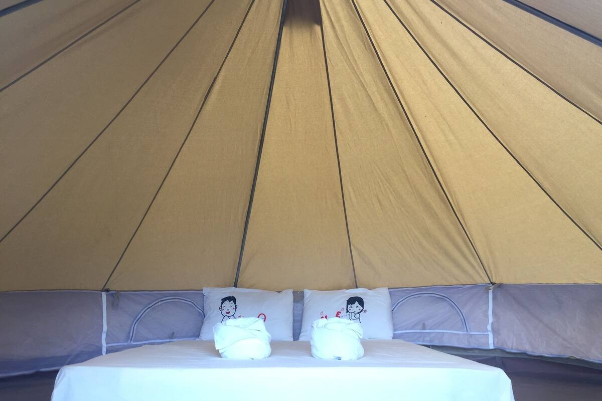 Uma tenda com uma cama por dentro, com duas almofadas de personagens de desenhos animados e um cobertor branco.