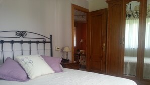Ein Bett mit Metallgestell, weißer Bettwäsche und zwei Kissen. Ein Holzschrank und eine Lampe auf einem Nachttisch sind ebenfalls zu sehen.