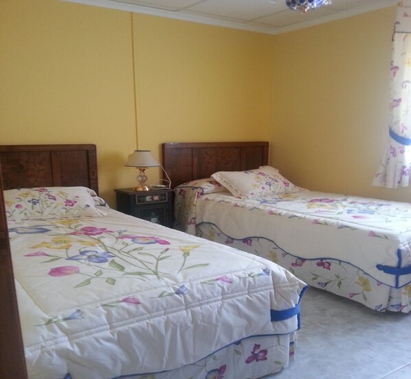 A room with two beds, each with floral bedding, a nightstand with a lamp, and a curtain on the window. - Carballo Blanco 2 Housing for Tourist Use (Celeiro de Mariñaos, Barreiros)