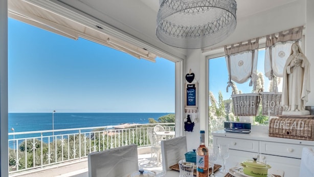A dining area with a view of the sea, a white table set with plates, glasses, and a purple pot. - Villa in Les Issambres near the Sea (Les Issambres)
