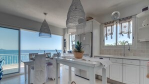 A spacious kitchen with white cabinets, a dining area with a table set for two, and large windows offering a view of the sea. - Villa in Les Issambres near the Sea (Les Issambres)