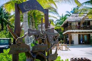 A wooden sign with various amenities including pet-friendly services, massage, tours, restaurant, bar, and bikes. - Casa Iguana Holbox (Isla Holbox)