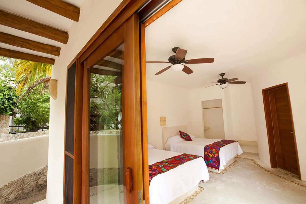A room with two beds, a ceiling fan, and a glass door leading to an outdoor area.