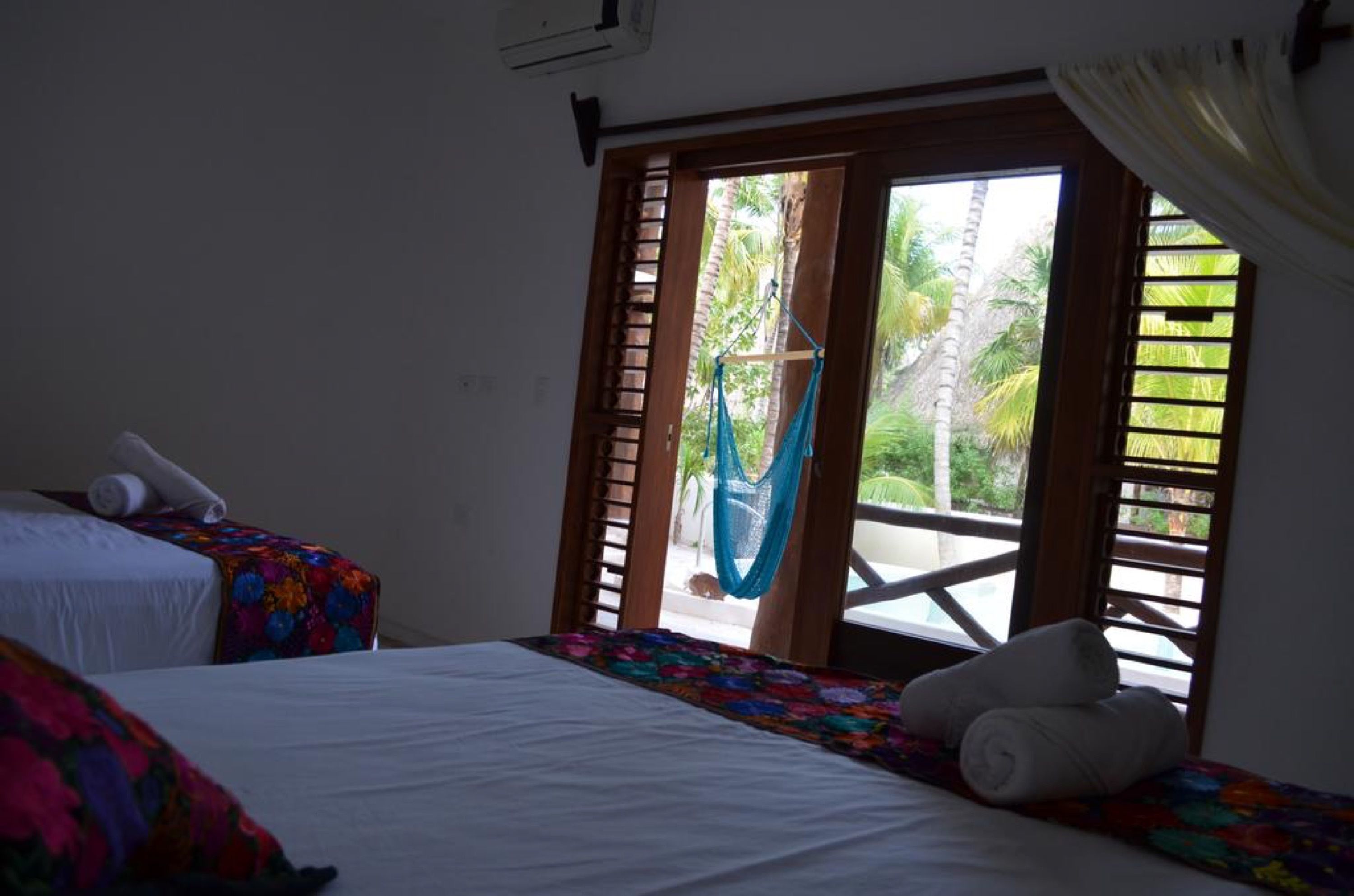 A room with two beds, a hammock, and a view of a balcony with palm trees.