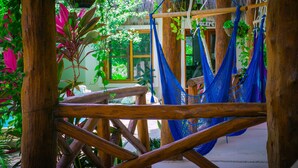 A wooden structure with hammocks suspended from it, surrounded by lush greenery and a thatched roof. - Casa Iguana Holbox (Isla Holbox)