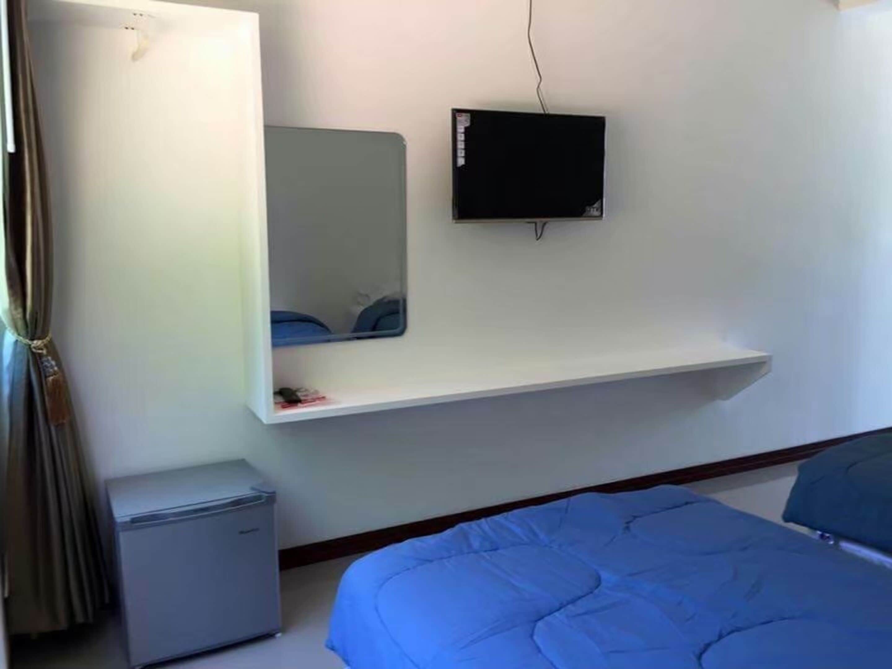 A bedroom with a bed, a small desk, a TV mounted on the wall, and a mirror.