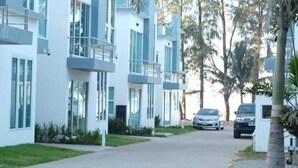 Un edificio residencial moderno de varios pisos con balcones, entrada para vehículos y automóviles estacionados.