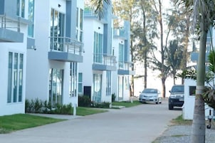 A modern multi-story residential building with balconies, a driveway, and parked cars.