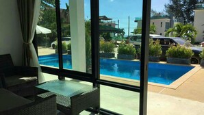 Habitación con un ventanal grande con vistas a una piscina, muebles de mimbre y vistas a la calle y edificios.