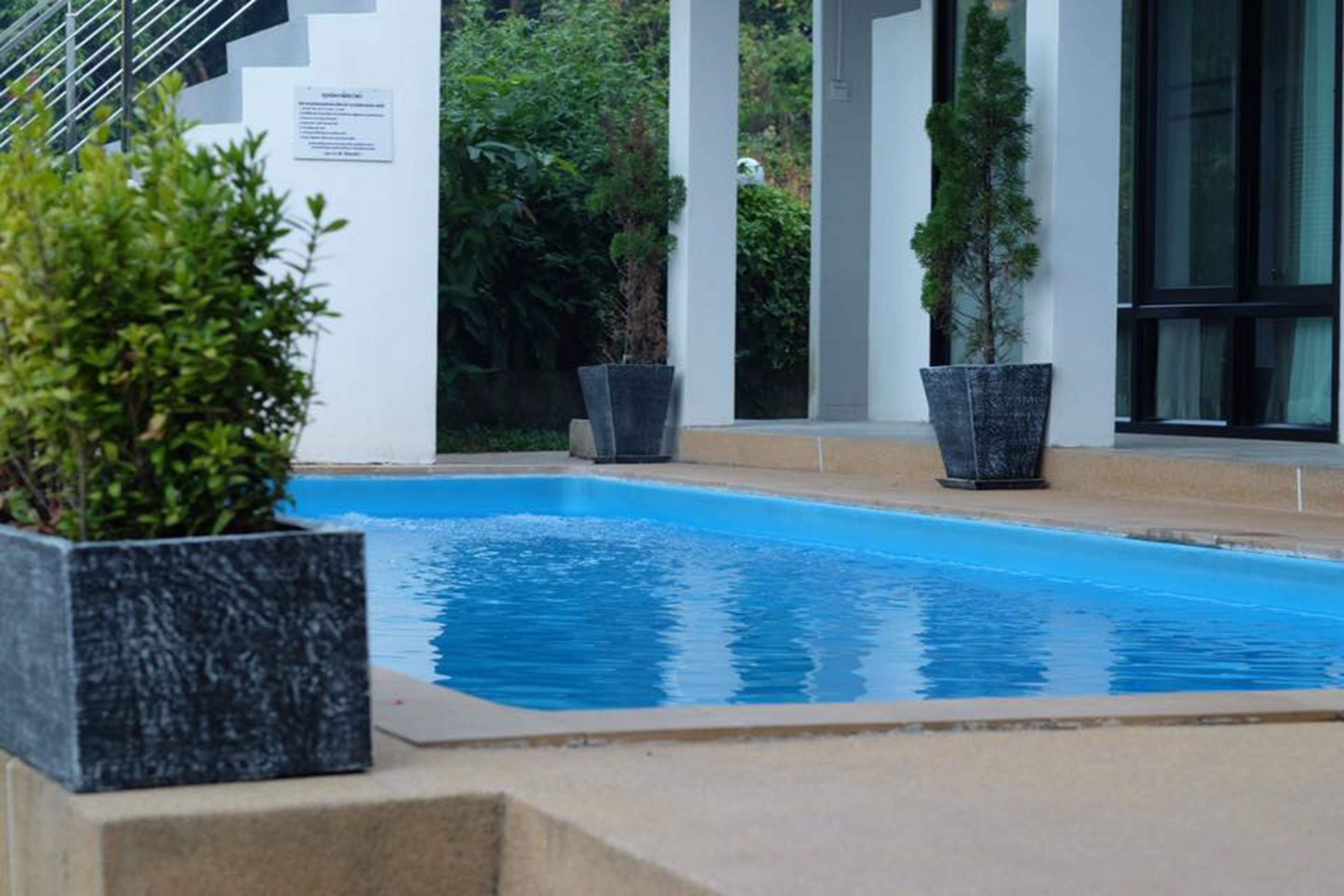 A swimming pool with a clear blue water, surrounded by white pillars and potted plants.