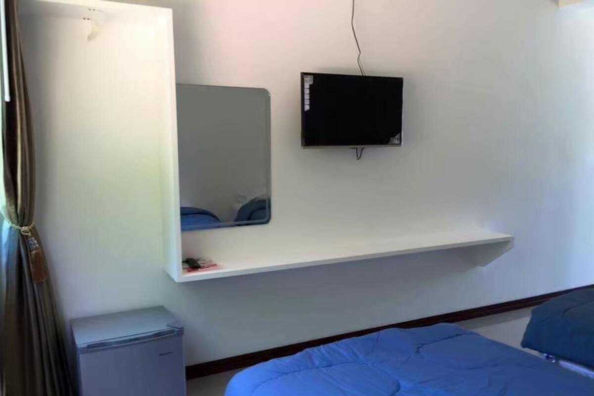 Une chambre à coucher avec un lit, un petit bureau, un téléviseur fixé au mur et un miroir.