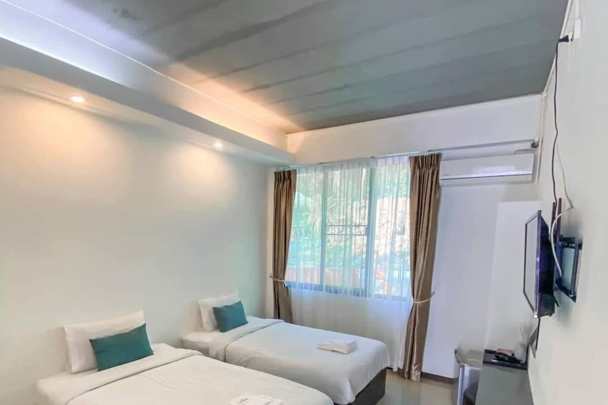 Une chambre d’hôtel avec deux lits, un téléviseur à écran plat fixé au mur et une fenêtre avec des rideaux.