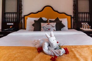 A neatly made bed with a white comforter, a decorative pillow with a bird pattern, and a white towel shaped like a rabbit with red flowers. - Manu Maharani Resorts (Ramnagar)
