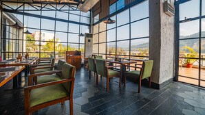 Un comedor amplio con grandes ventanales que ofrecen vistas al exterior. Las mesas y sillas están dispuestas para comer.